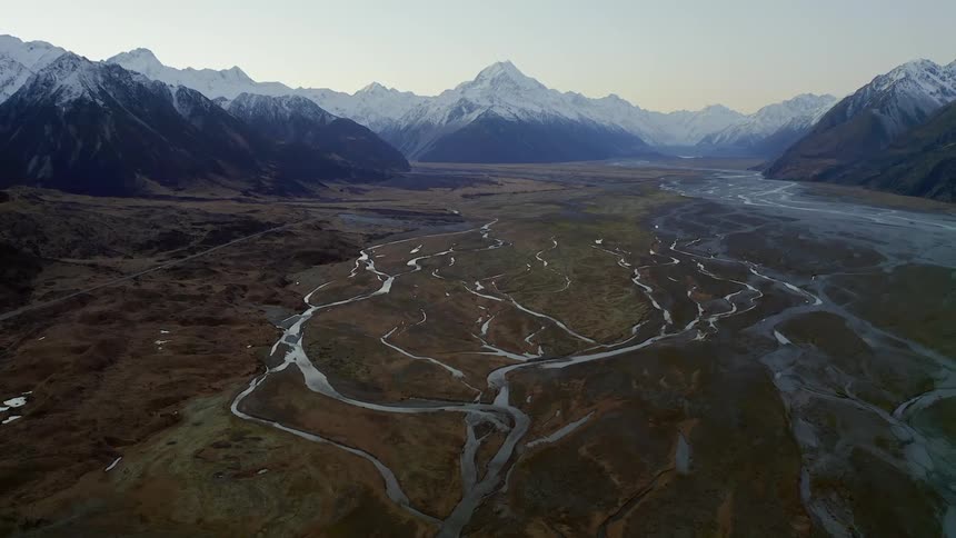 Small winding streams running through land surrounded by snowy mountains