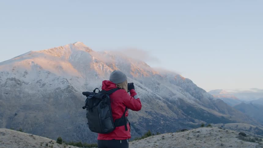 Woman with a backpack takes a photo of the snow covered mountains