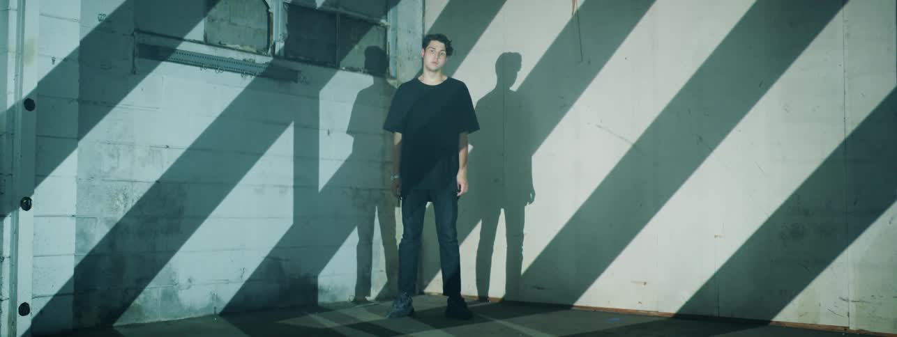 Man in a black shirt stands in a corner as shadows move over him