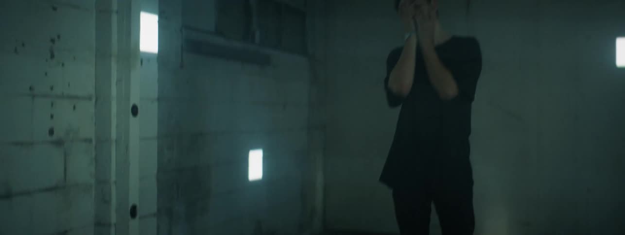 The man rubs his face and walks backwards in the room with flashing lights