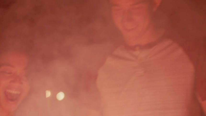 The fireworks are giving off smoke as the people smile together at night