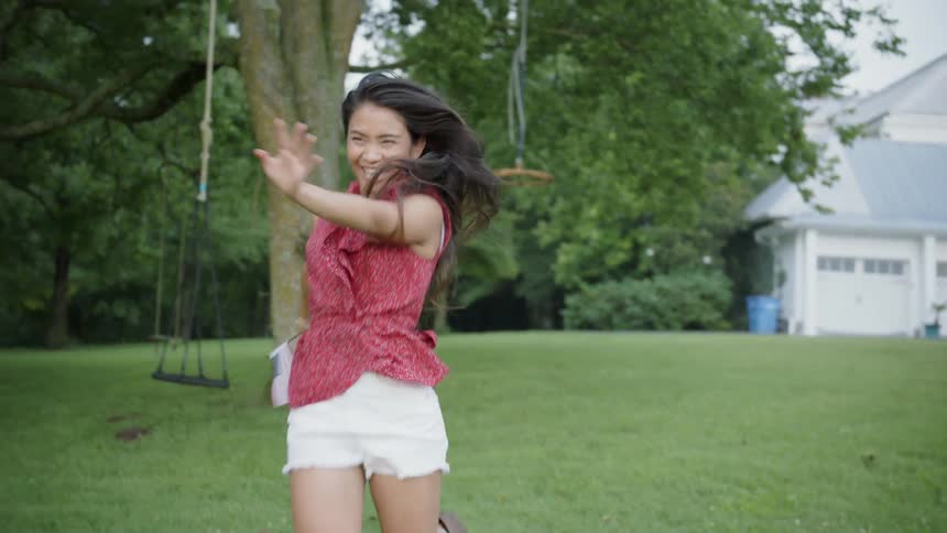 A woman is waving a flag and smiling as she runs across a lawn in daylight