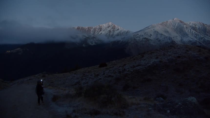 A person hikes in snowy mountains with a headlamp at night
