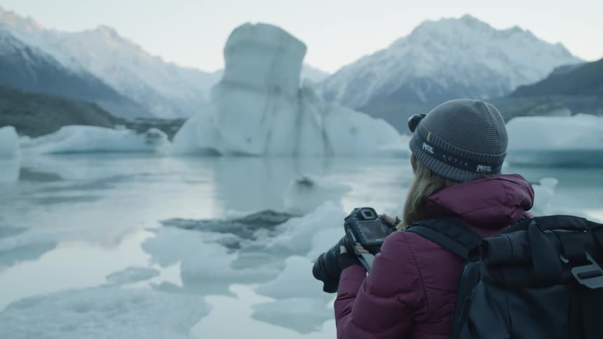 A woman is taking photos of icebergs with an slr camera in daylight