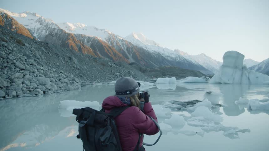 Woman is photographing icy lake in snowy mountain wilderness