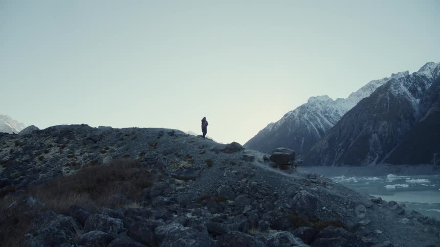 A person with a backpack descending a rocky trail with mountains in the background