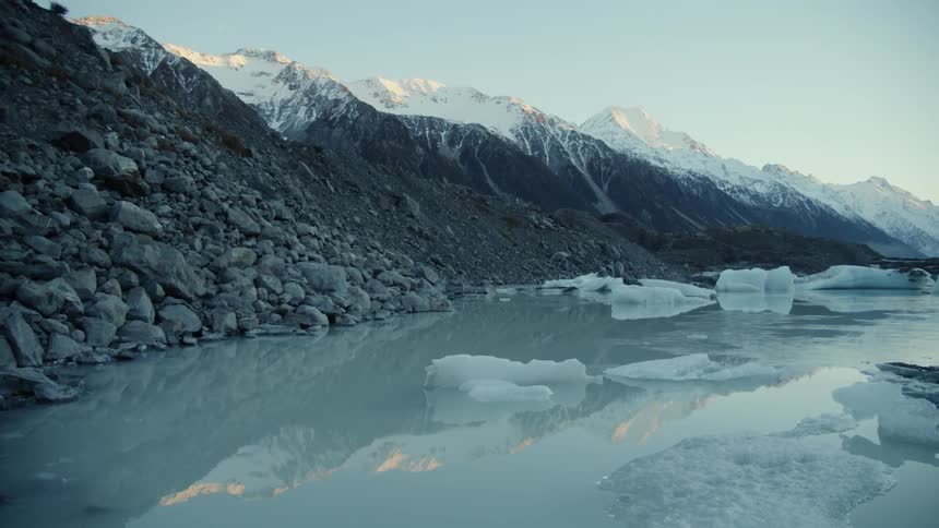 Chunks of ice floating in water next to a rocky mountain on a bright day