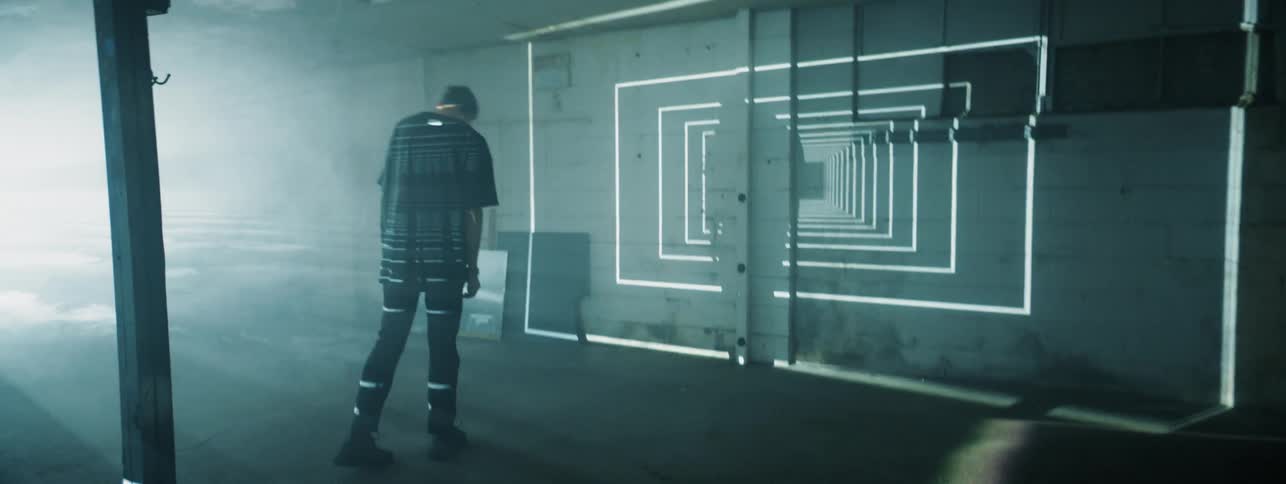 Lights are projected onto a wall behind a man in a dark room