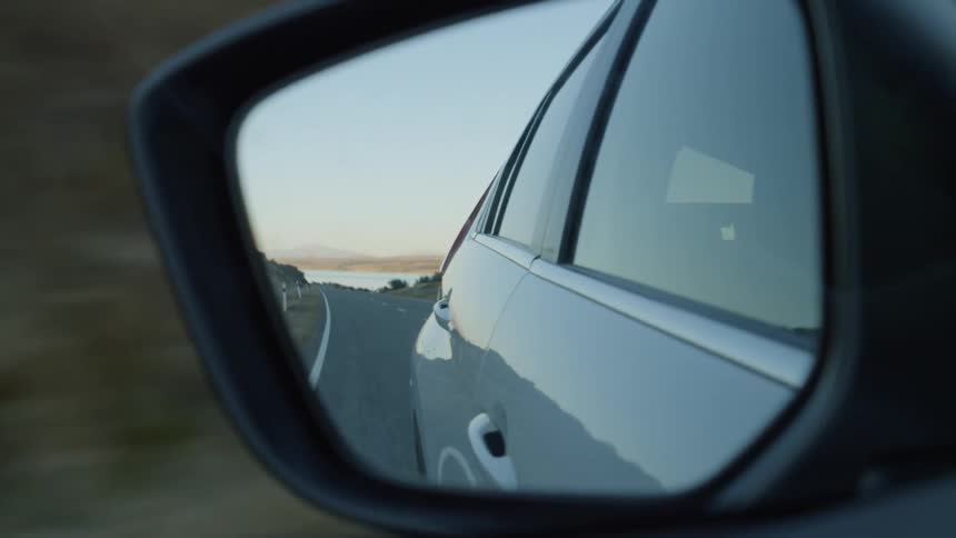 The rearview mirror shows the road behind the moving car