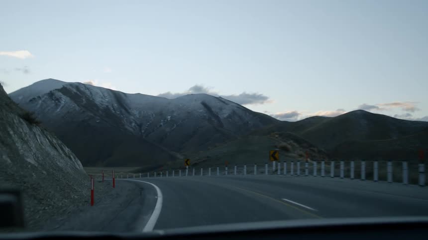 Car traveling on highway in front of snowy mountains after sunset