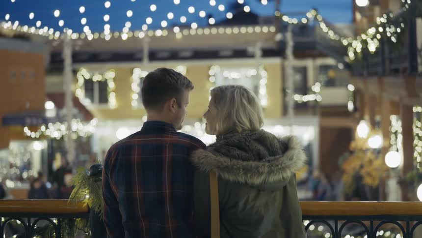 Man kissing a woman's forehead under christmas lights