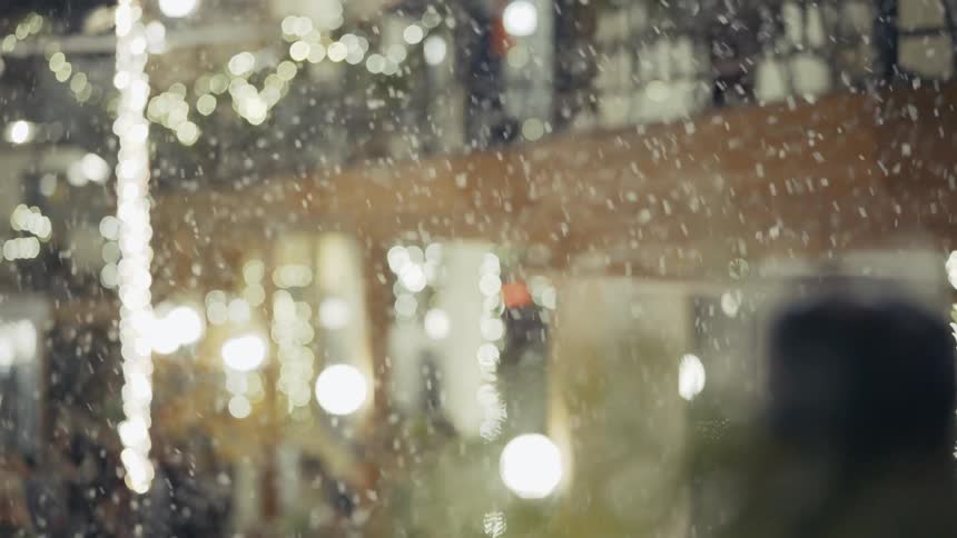 Snow falls gracefully on a street lit by christmas lights