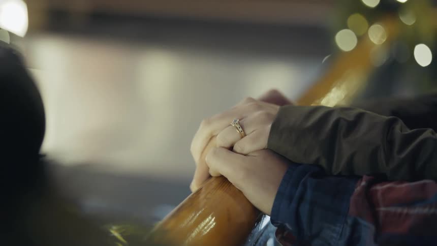 A man is holding hands with a woman with a wedding ring on her hand while they hold onto a railing