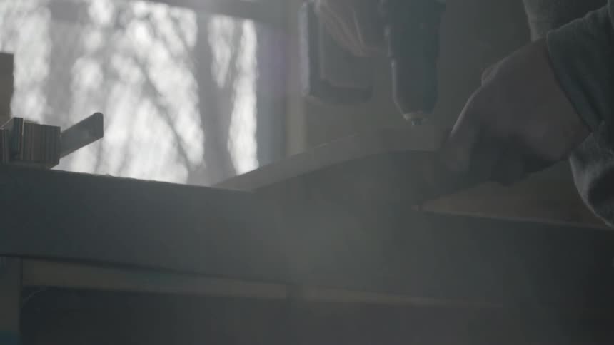 A man holds a wooden board while he drills a hole through it