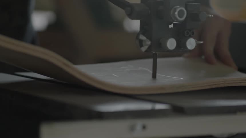 A person uses a table jig saw to cut out an outline on a warped piece of plywood
