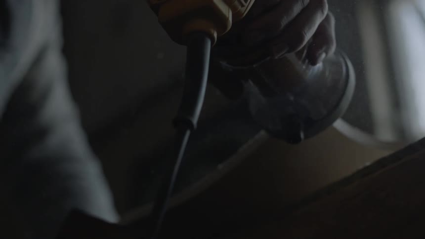 A man moves a sander over to a wood board