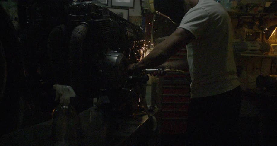 A worker grinds now some metal in a dark shop