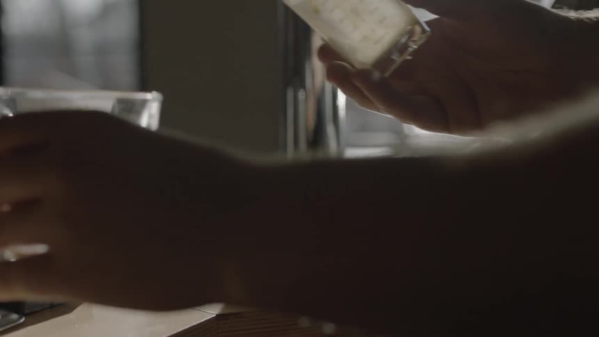 A man pours a small glass into his larger glass then cleans it on the bar