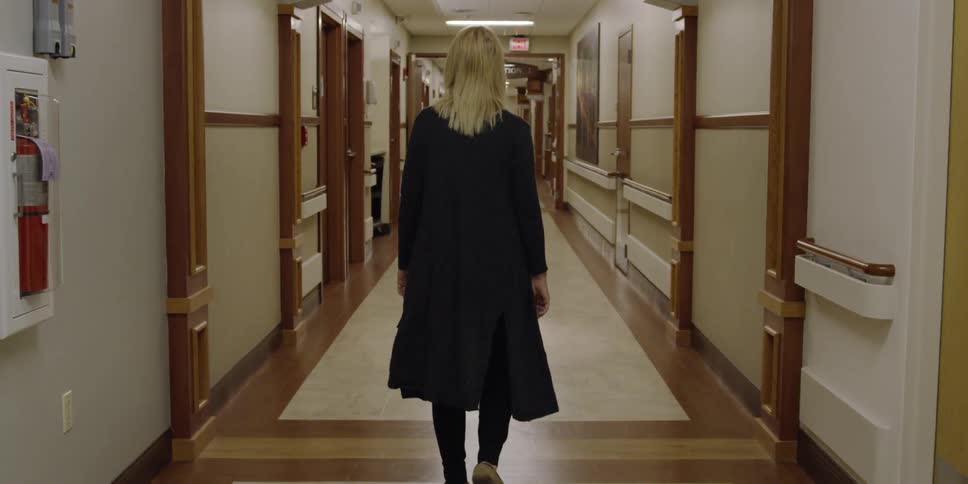 A woman in all black walks down a long hallway
