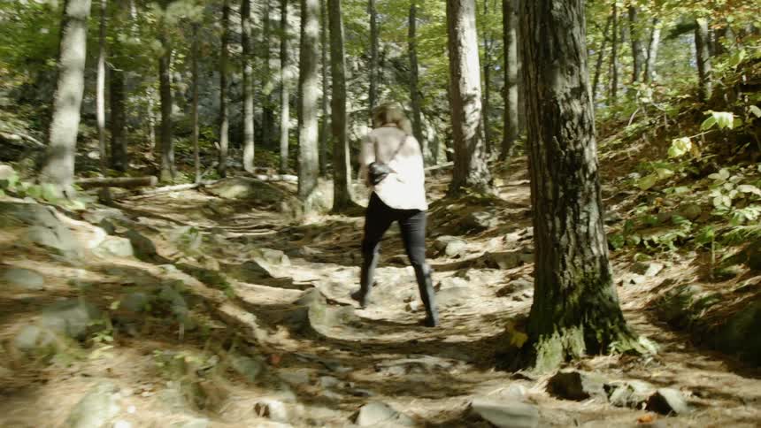 A woman walks up a rocky hill surrounded by trees in a forest