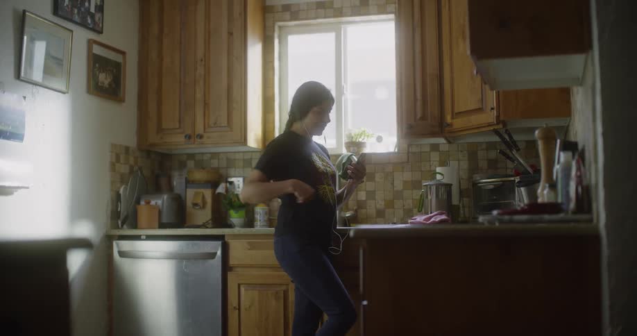 Woman standing in a kitchen picks up her phone and looks at i