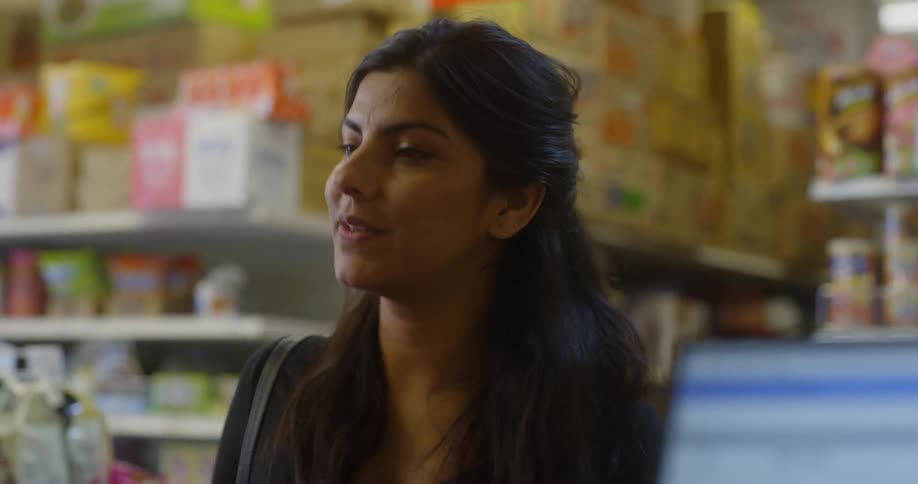 A woman sets her shopping basket on the counter and hands an item to a cashier that we cannot see