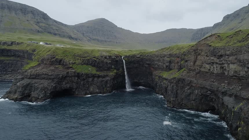A waterfall flows into the ocean from atop a cliff