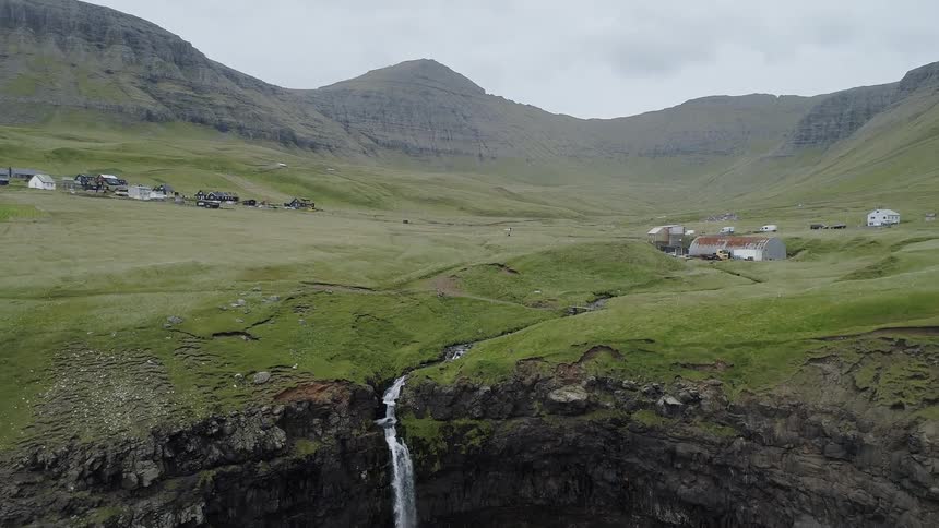 A waterfall that is at the edge of a cliff in a mountain region