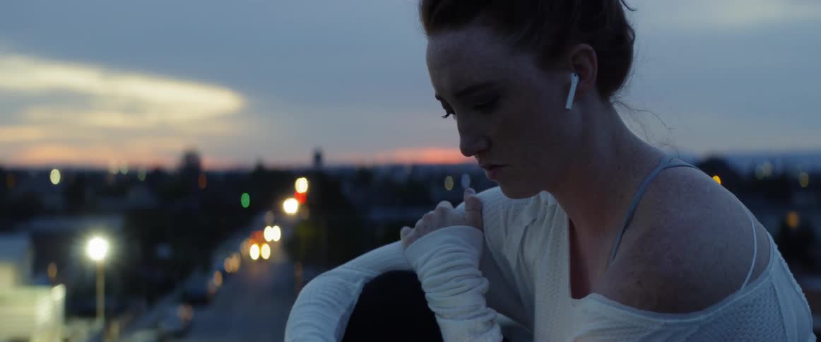Woman wearing earphones looking at her phone on top of a roof in a city