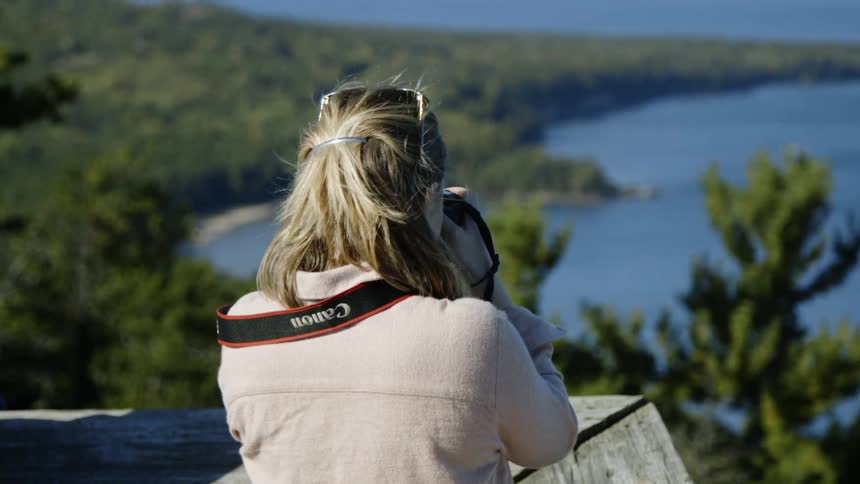 Woman taking a picture of a large body of water next to the forest