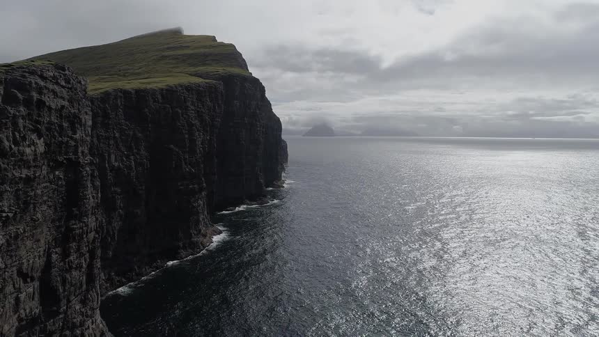 Water flows around a tall cliff on a cloudy day