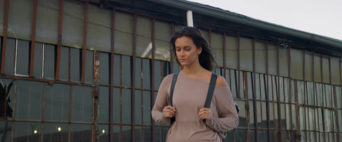 A woman wearing a backpack walks past an old building