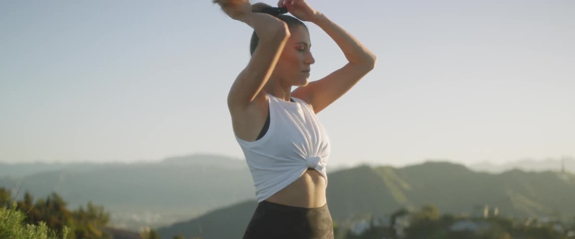 A woman wearing exercise clothes puts her hair into a high ponytail