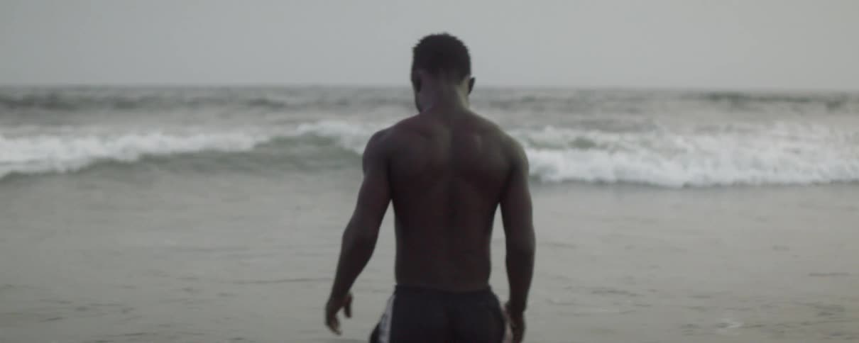 A shirtless man wades into the ocean as waves flow around him