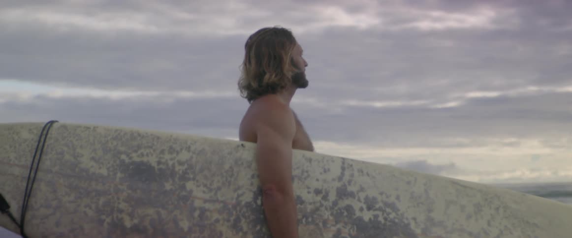 A man standing at the beach holding a surfboard
