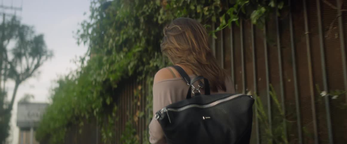 A young woman carrying a backpack walks by a fence