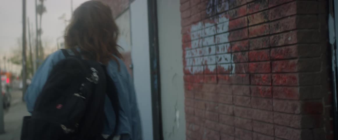 A woman wearing a backpack walks out of a house and down the street