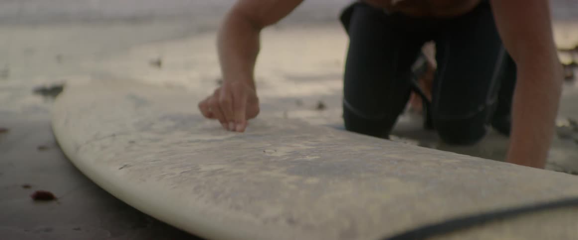 Man kneeling down at his surfboard and rubbing it