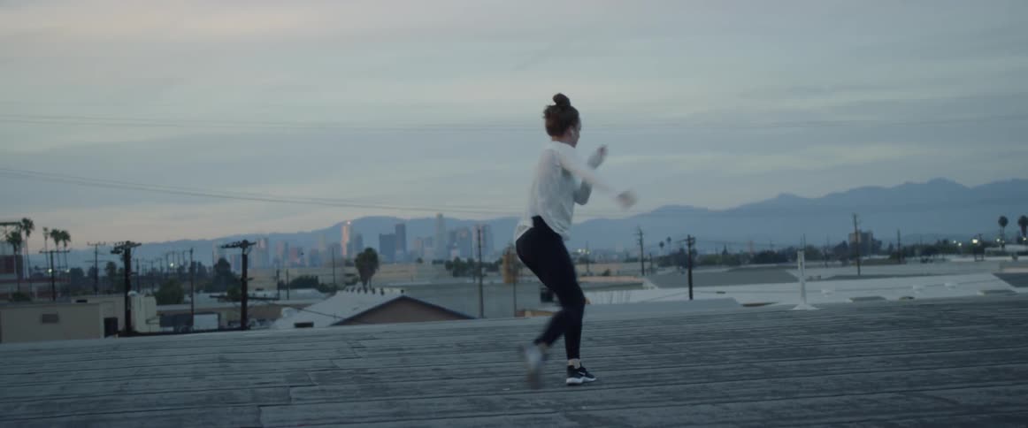 A girl in a white shirt dances on a rooftop