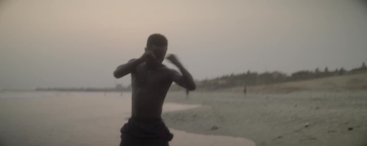 A man practices boxing on a beach at sunset
