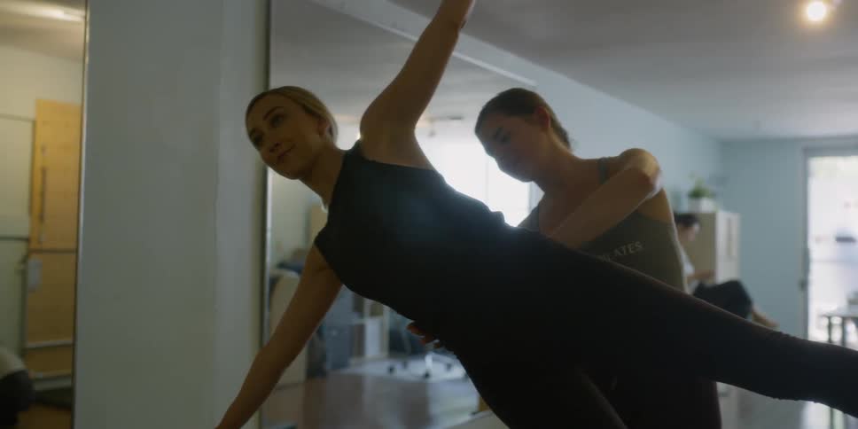 Woman helps another woman practice a yoga pose