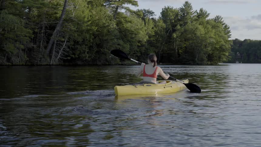 A woman is rowing a kayak down a river