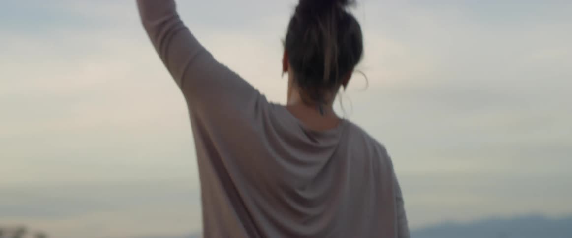 A woman wearing wireless earbuds dances in the sunset