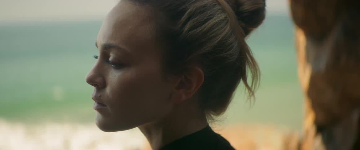 A woman stands in front of water as she closes her eyes and thinks