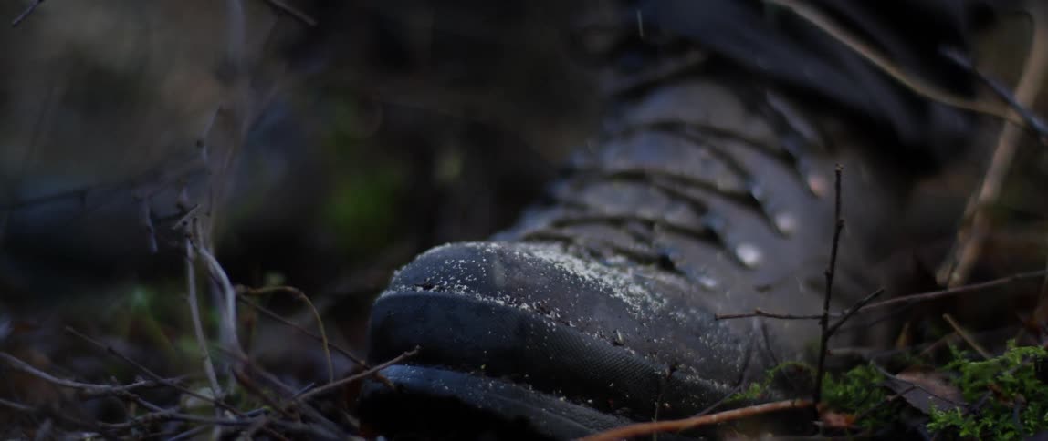 Snow falling on a boot stepping on the forest ground