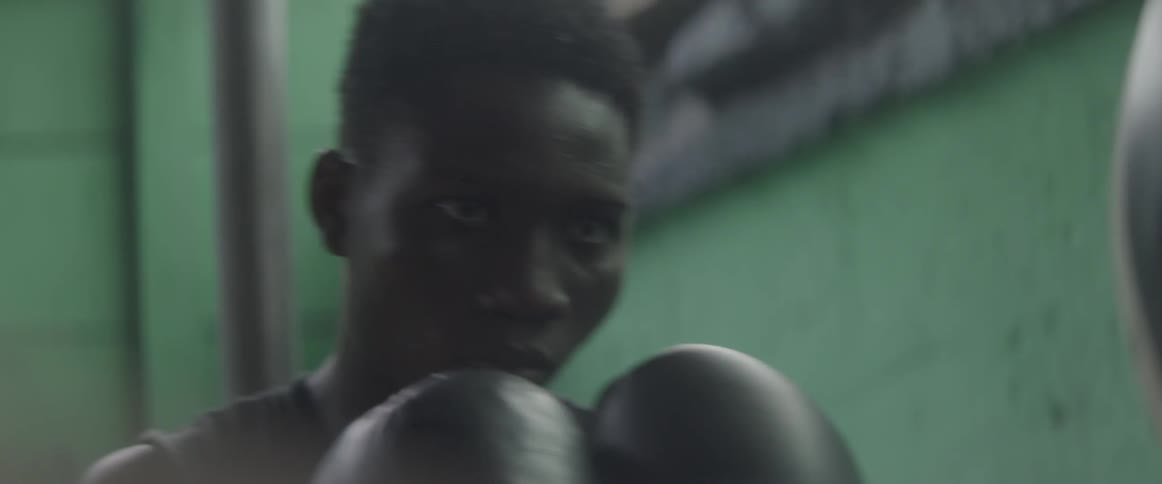 A man with boxing gloves on bobs and weaves as he punches a speed bag
