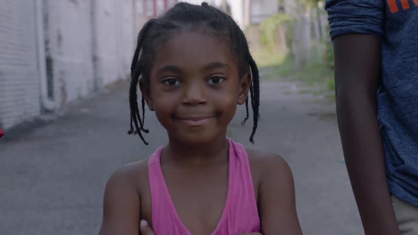 A young girl stands in an alley and smiles