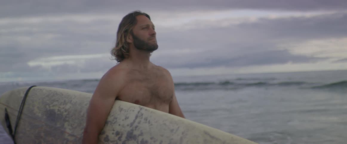 A surfer carries his surfboard on the beach