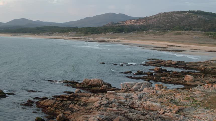 Waves crash onto a rocky beach that leads up to small hilltops