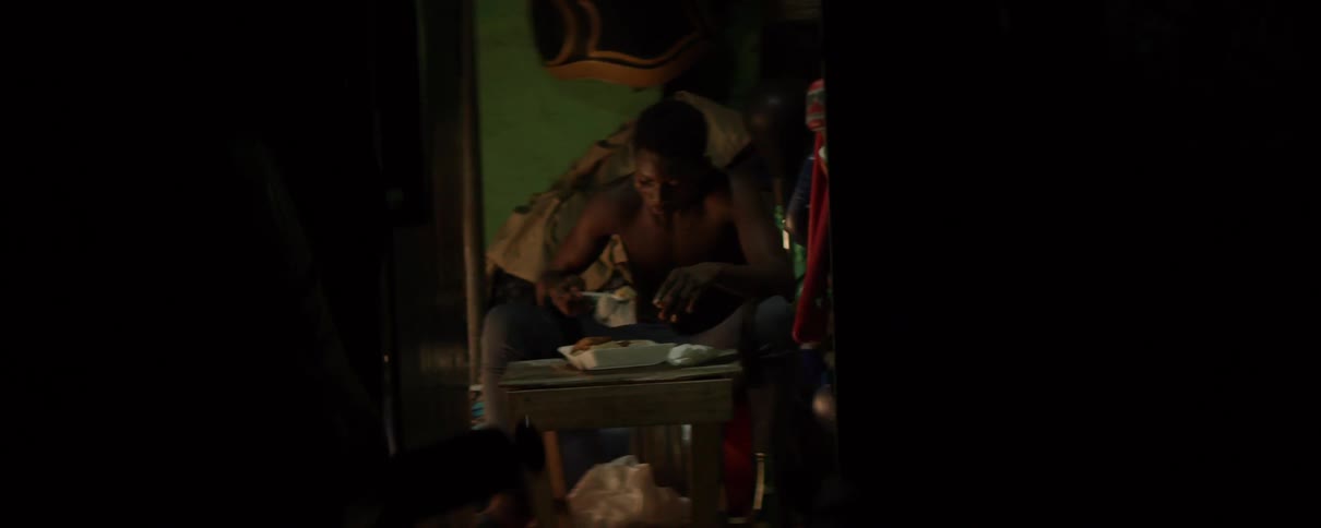 A man sits alone in the darkness eating off of a spoon from a styrofoam container